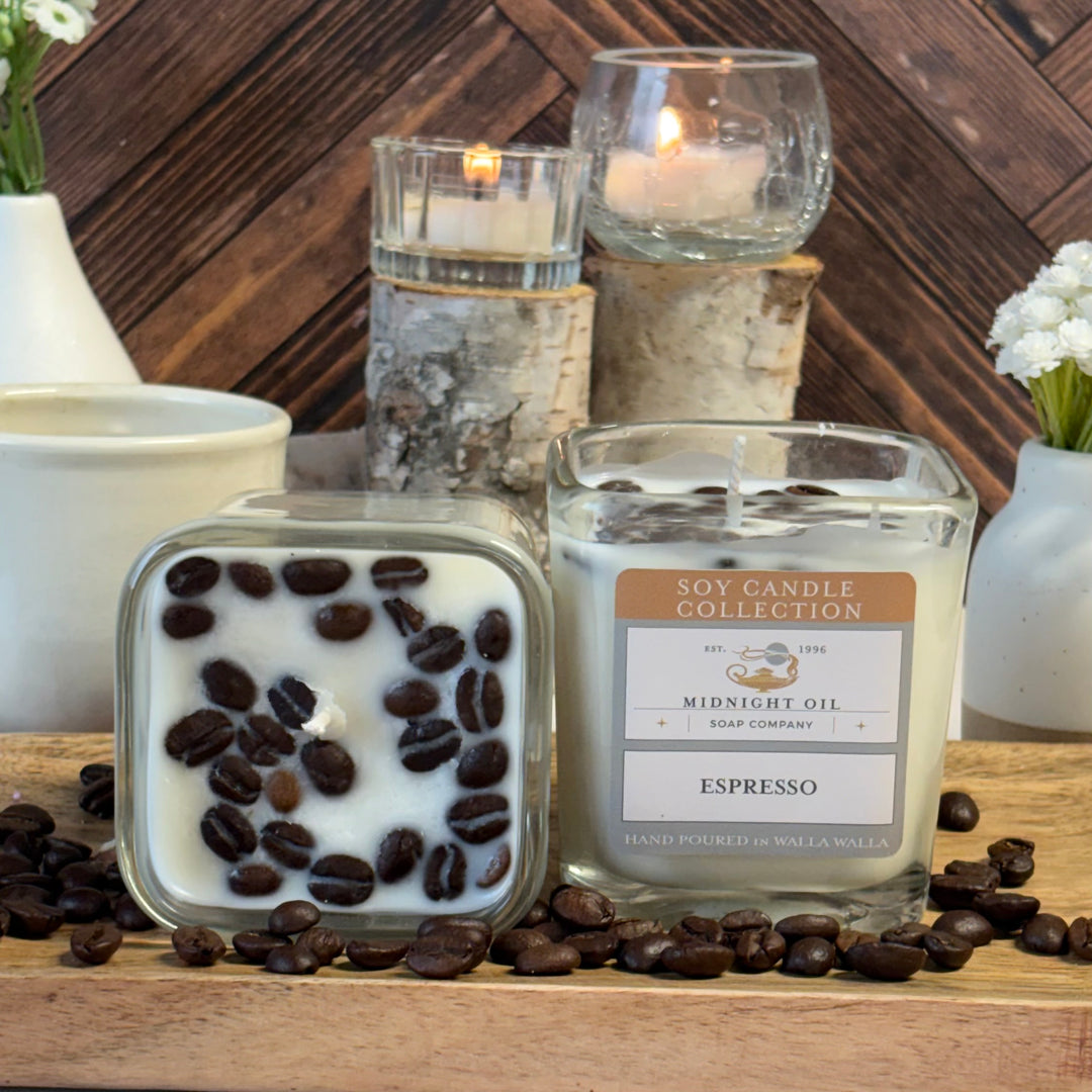 Candle with coffee beans and 'Espresso' label on a wooden surface with other candles and decor. MIDNIGHT OIL SOAP