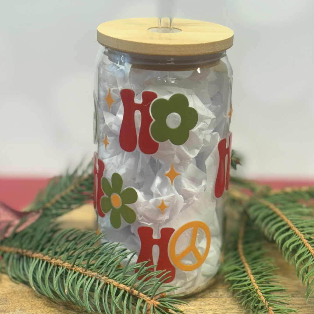 Clear tumbler with floral designs and wooden lid on a wooden surface with greenery