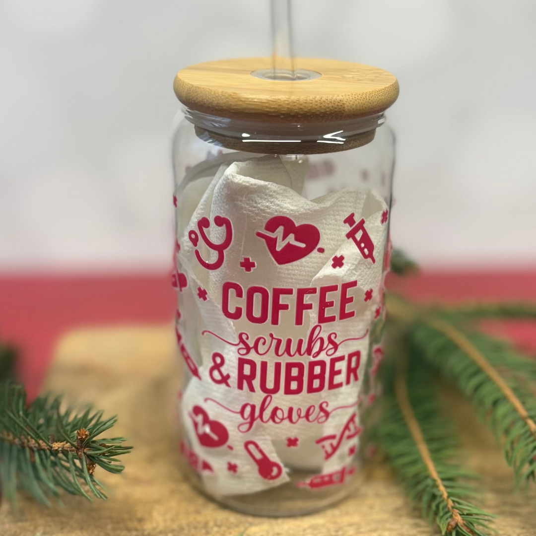 Glass tumbler with wooden lid and straw, featuring text and graphics, on a wooden surface with greenery.